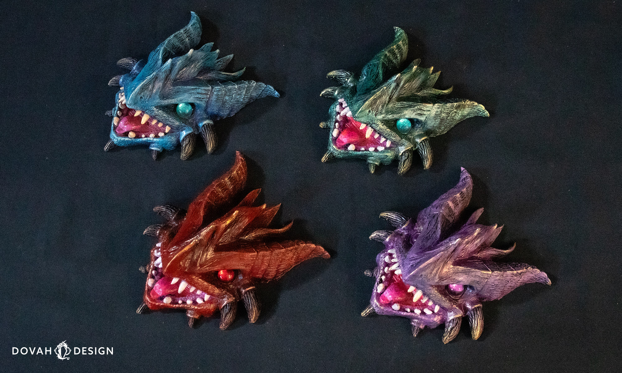 Four dragon wall decor sculptures in blue, red, purple, and green, sitting on a black table.