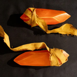 Two orange guidance soapstones, sitting on a black background, placed horizontally to the camera, with their yellow painted fabric flowing away from each stone.