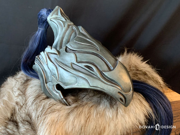 Finished resin cast helmet of Knight Artorias, made by Dovah Design. Helmet sitting on top of a wooden box with white fur padding, faced right with the blue wig hair folded beneath.