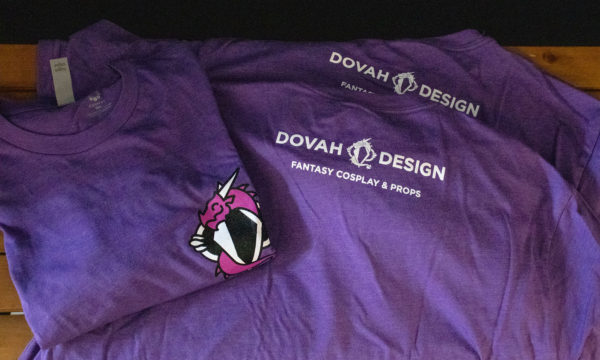 Close up detail of the Dovah Design t-shirt, a folded shirt sitting on top of two flat shirts showing the back design.