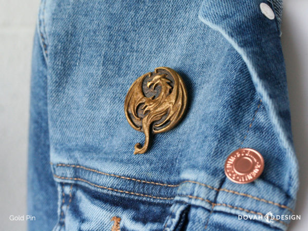 Elsweyr dragon logo lapel pin in gold, pinned on a jean jacket for scale, close up detail shot of the cast resin pin.