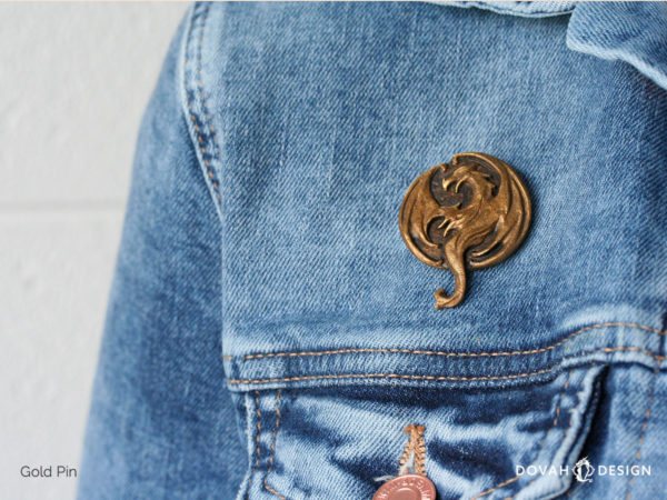 Elsweyr dragon logo lapel pin in gold, pinned on a jean jacket for scale, close up detail shot of the cast resin pin.