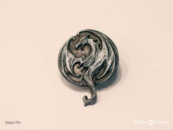 Shiny steel lapel pin, cast in resin, of the Elder Scrolls Online Elsweyr logo. Close up detail of the dragon logo, sitting on a white background.