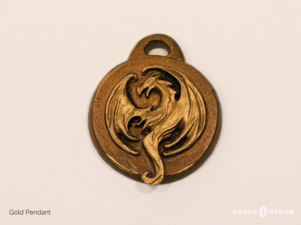 Elder Scrolls: Online Elsweyr logo, gold resin cast pendant. Shown lying flat. Logo depecits a dragon or drake in metallic gold.