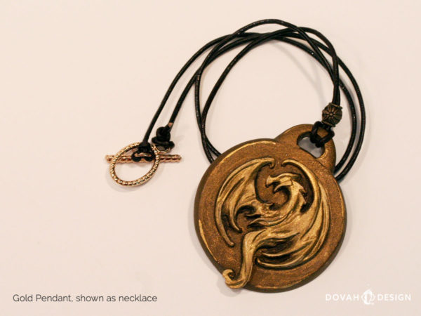 Elder Scrolls Online Elsweyr logo, gold resin cast pendant necklace. Shown lying flat. Logo depecits a dragon or drake in metallic gold.