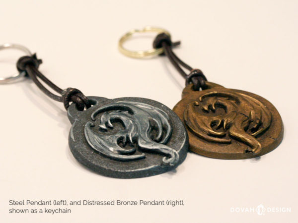Steel and bronze Elder Scrolls Online Elsweyr logo pendants. Shown tied as a keychain (keyring) lying flat. Logo depecits a dragon symbol.
