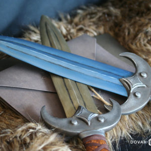 Two prop khajiit daggers posed crossed at the blade over top of a book bound with twine. Top dagger, "Jone," in voidsteel (blue). Bottom dagger, "Jode" in calcinum (gold).