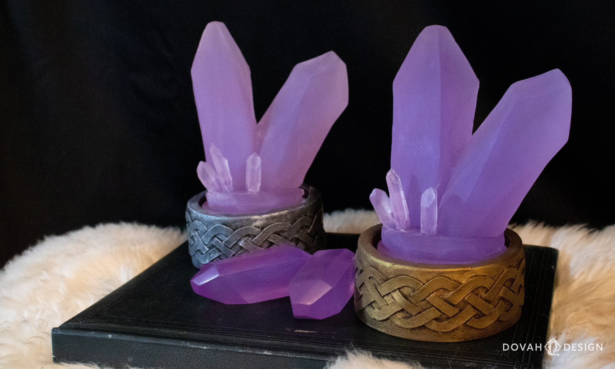 Two grand soul gem desk lights, shown unlit sitting on a black book atop white fur, with a black background.