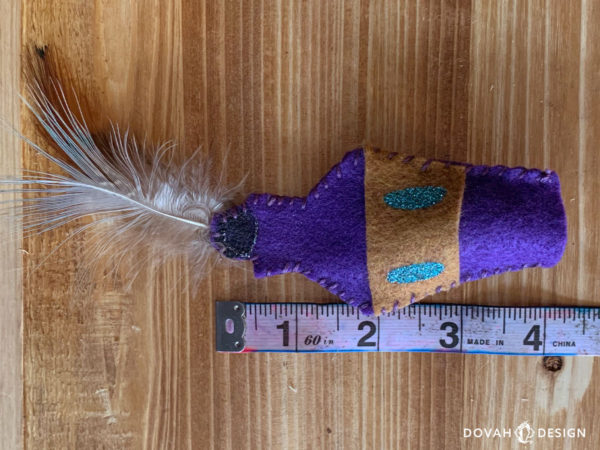 Handmade skooma bottle cat toy on a wood table, with soft ruler laid out for measurement. Felt portion of toy measures approximately 4 inches.