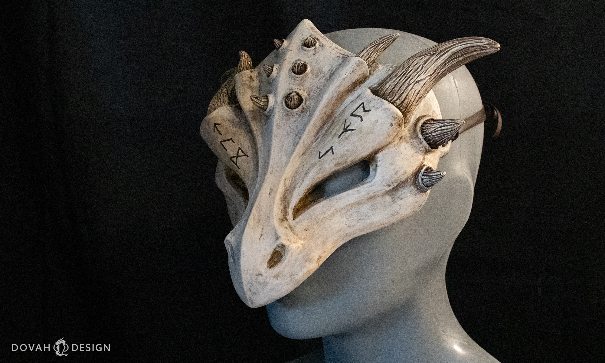 Resin dragon mask with elder futhark runes carved over the eyes, viewed on a gray mannequin head facing left with a black background.