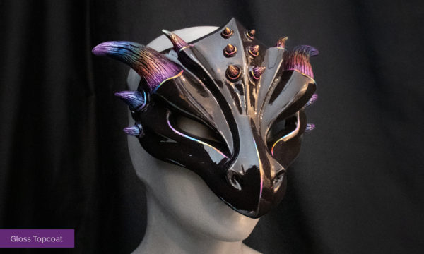 Glossy rainbow dragon mask. Masquerade style mask has a black face and rainbow gradient up the horns. Mask is finished with high gloss enamel topcoat, seen tied on a mannequin bust in front of a black background.