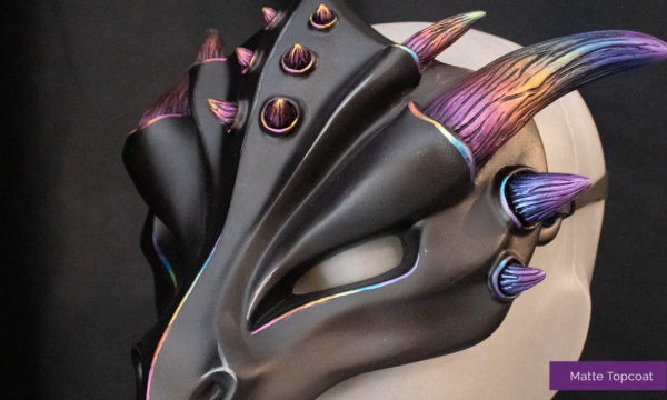 Detailed close up of the rainbow dragon mask. Mask has a black face with rainbow horns and matte finish, tied on mannequin bust, facing left.