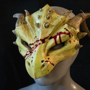 Halloween zombie dragon mask, "masquerade style," cast in yellow green urethane resin with red epoxy blood splatter, facing left on a black background.