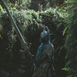 Sam in her Knight Artorias cosplay, holding the Greatsword of Artorias in a dark, green garden resembling Oolacile.