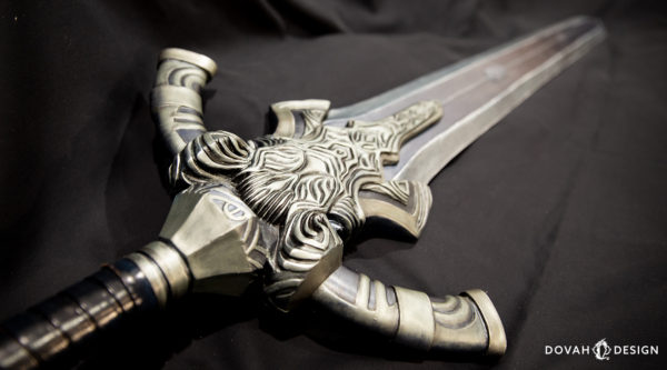 Finished and painted prop greatsword of Artorias, laying on a table draped with a black sheet, close up detail of the sculpted hilt.