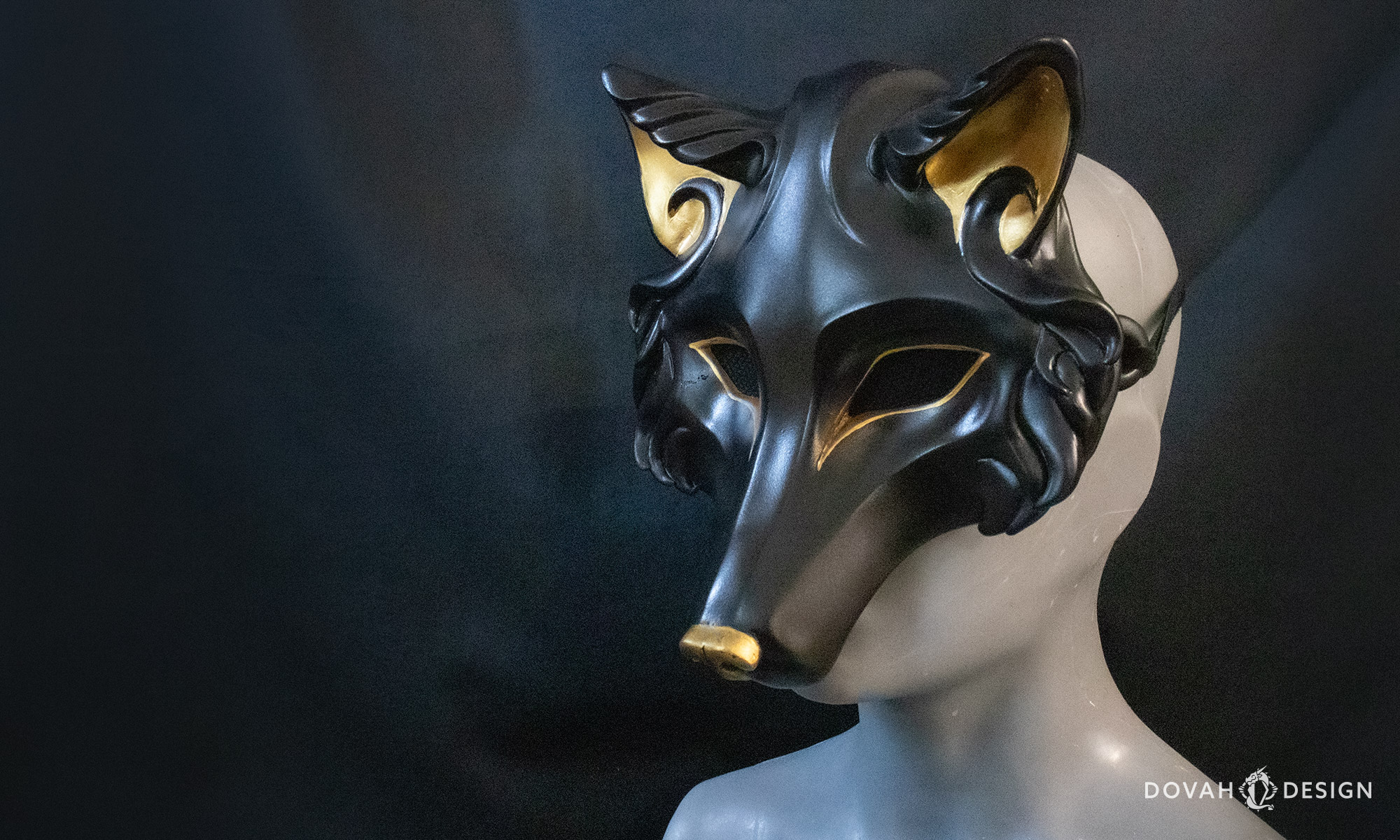 Side 3/4 view of a black wolf mask with gold inner ears, eyes, and nose, similar to an Egyptian Anubis, shown on a mannequin in front of a black background.