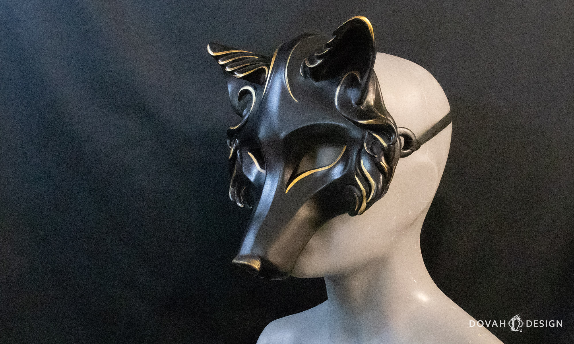 Angled view of a black masquerade wolf mask with gold details painted, shown tied on a mannequin bust in front of a black background.