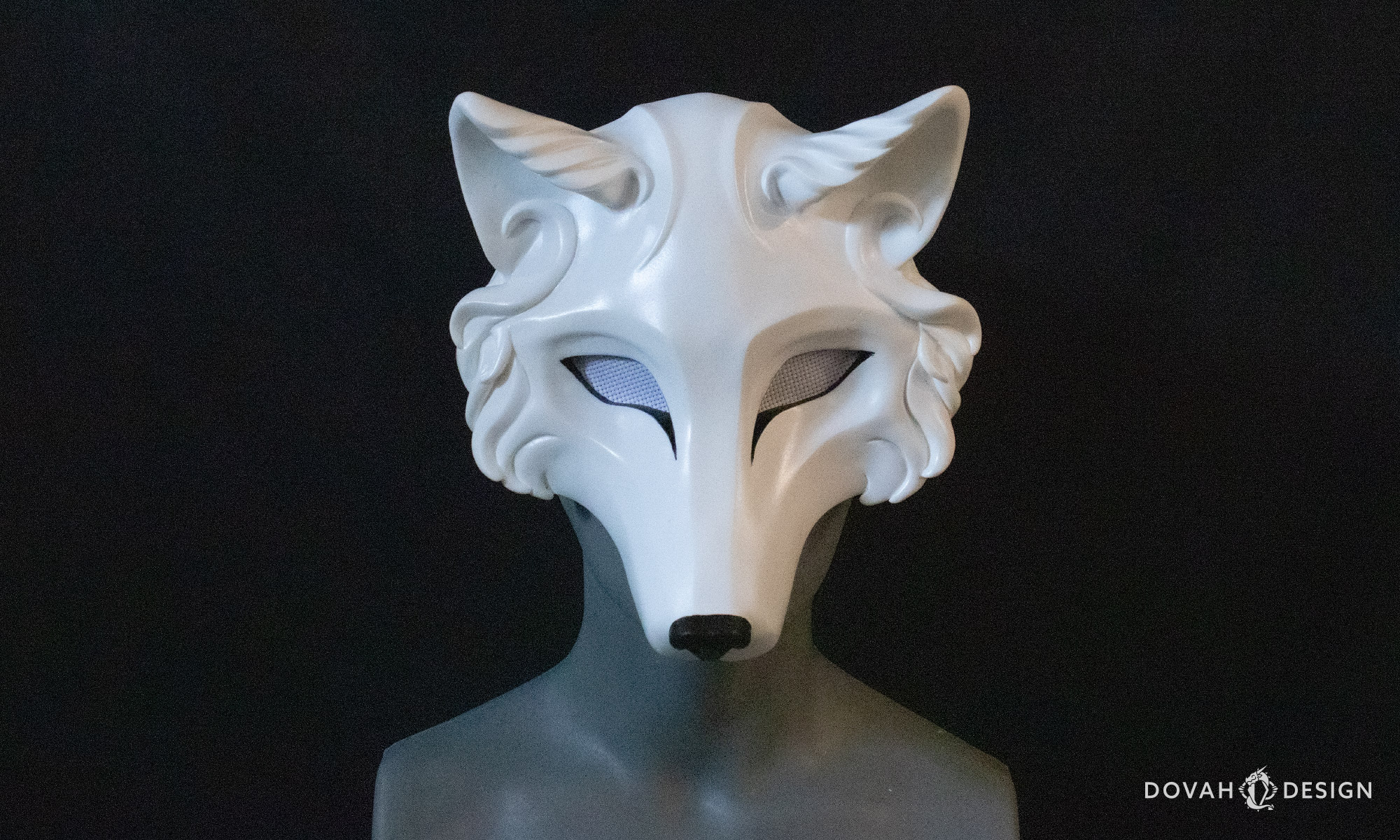White masquerade wolf mask with painted black eyeliner and black nose, eye holes covered in white mesh, posed on a mannequin in front of a black background.