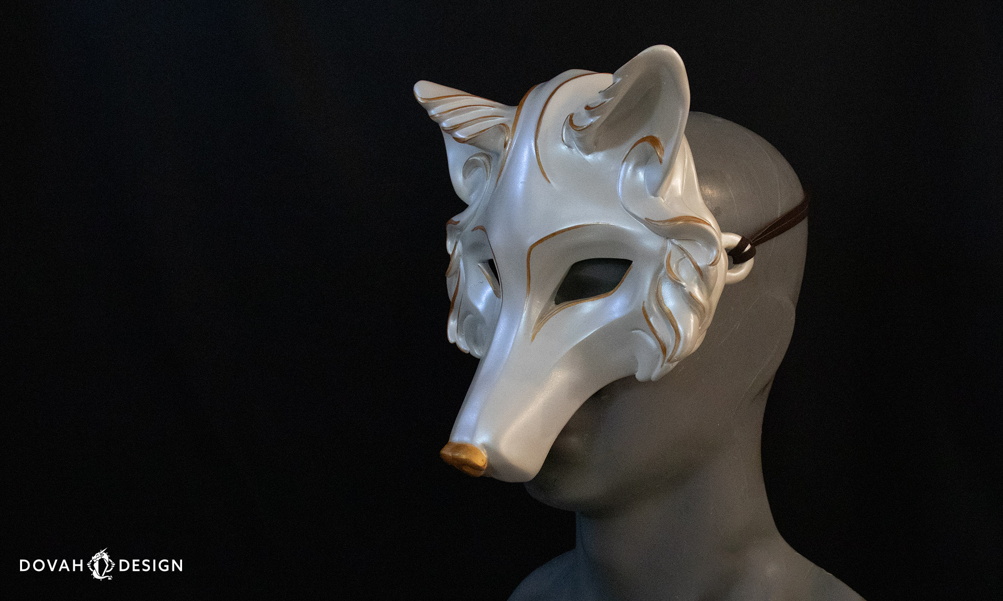 Three quarter right angle of a white wolf mask with gold hand painted details visible.